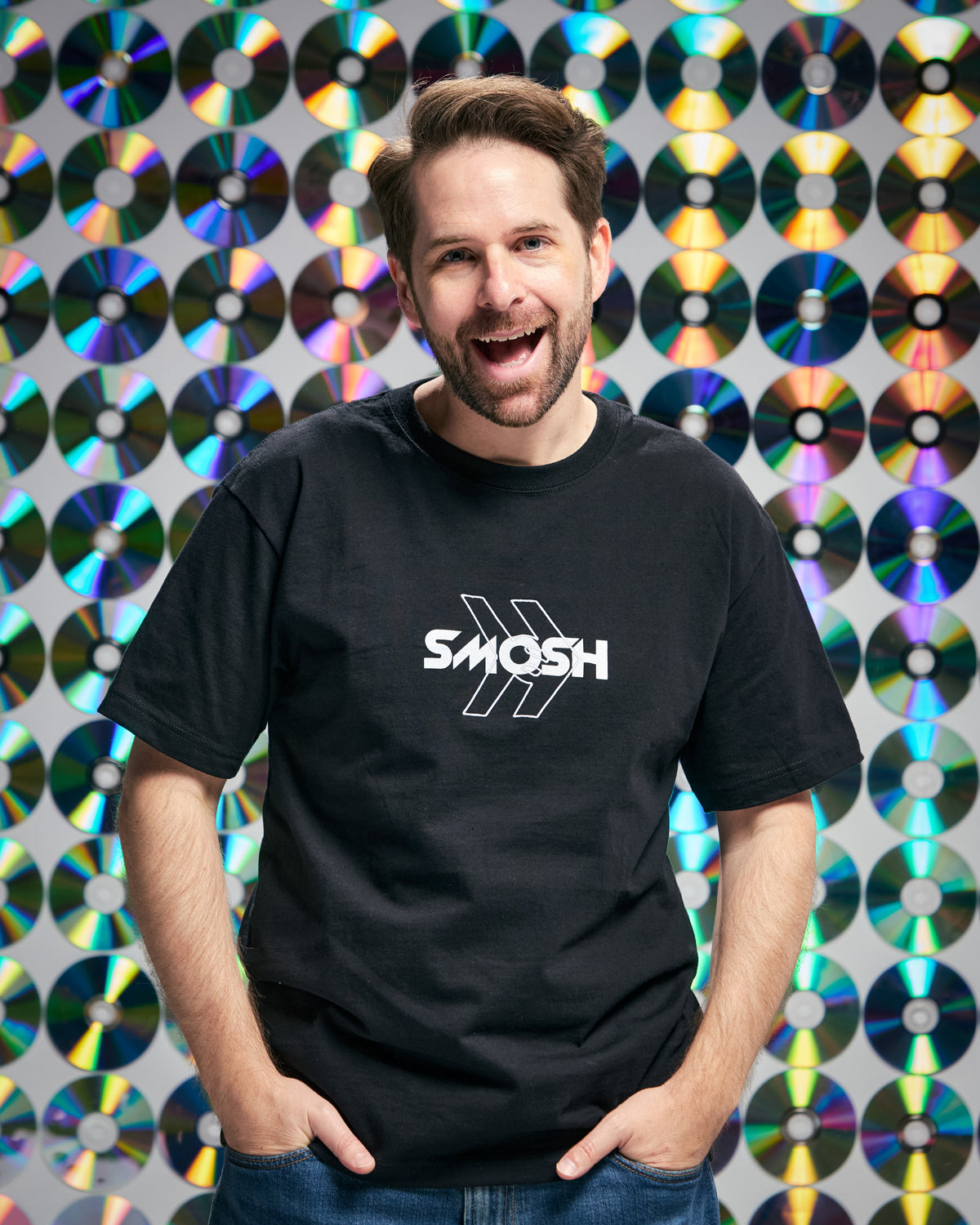 Person wearing a black t-shirt with a Smosh logo in front of a colorful disc pattern