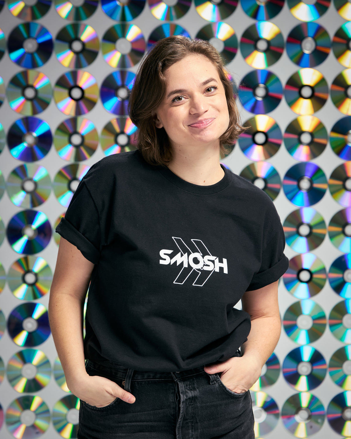 Person wearing a black t-shirt with 'Smosh' logo in front of a colorful CD pattern background
