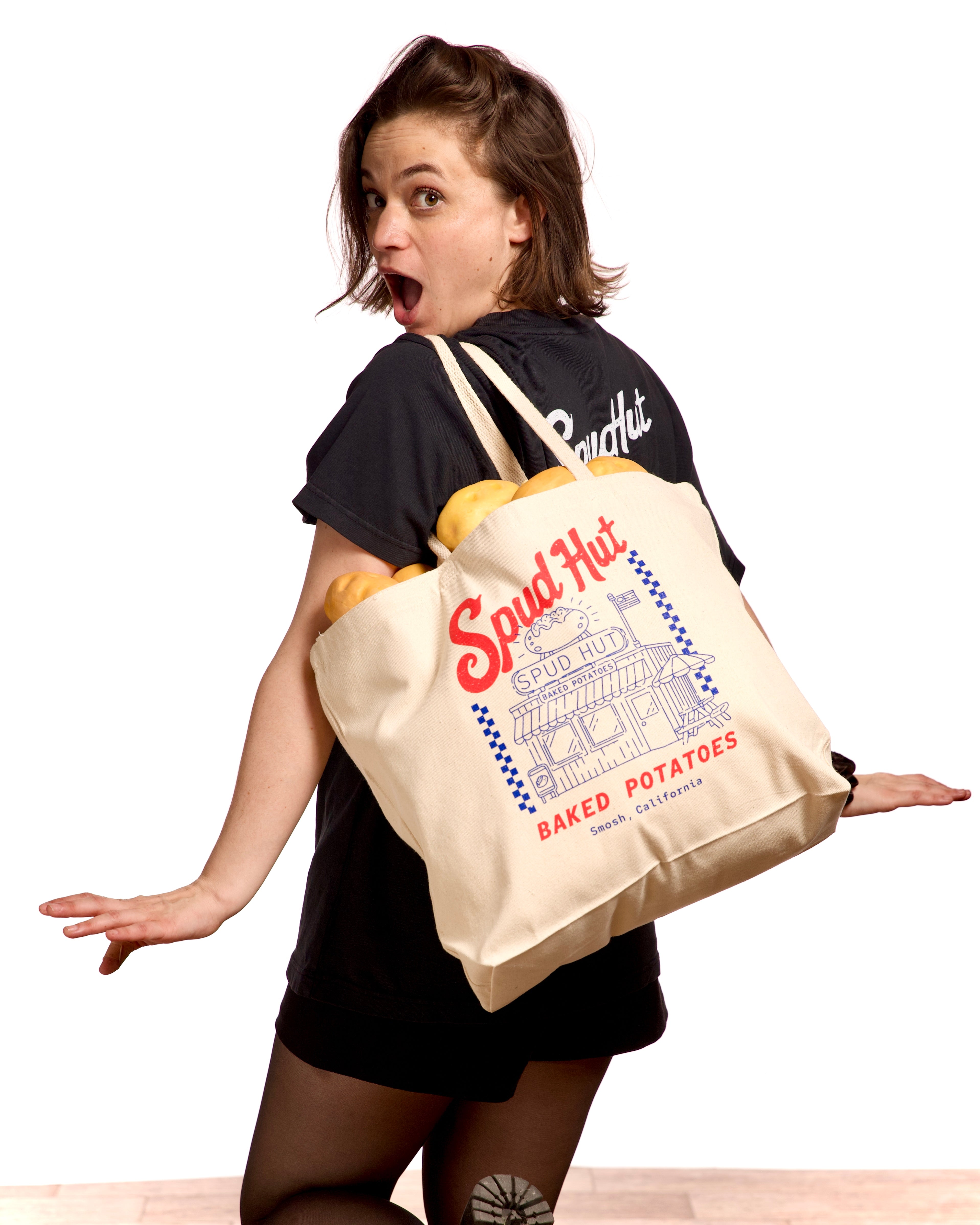 Woman carrying a Spud Hut tote bag with potatoes on a white background