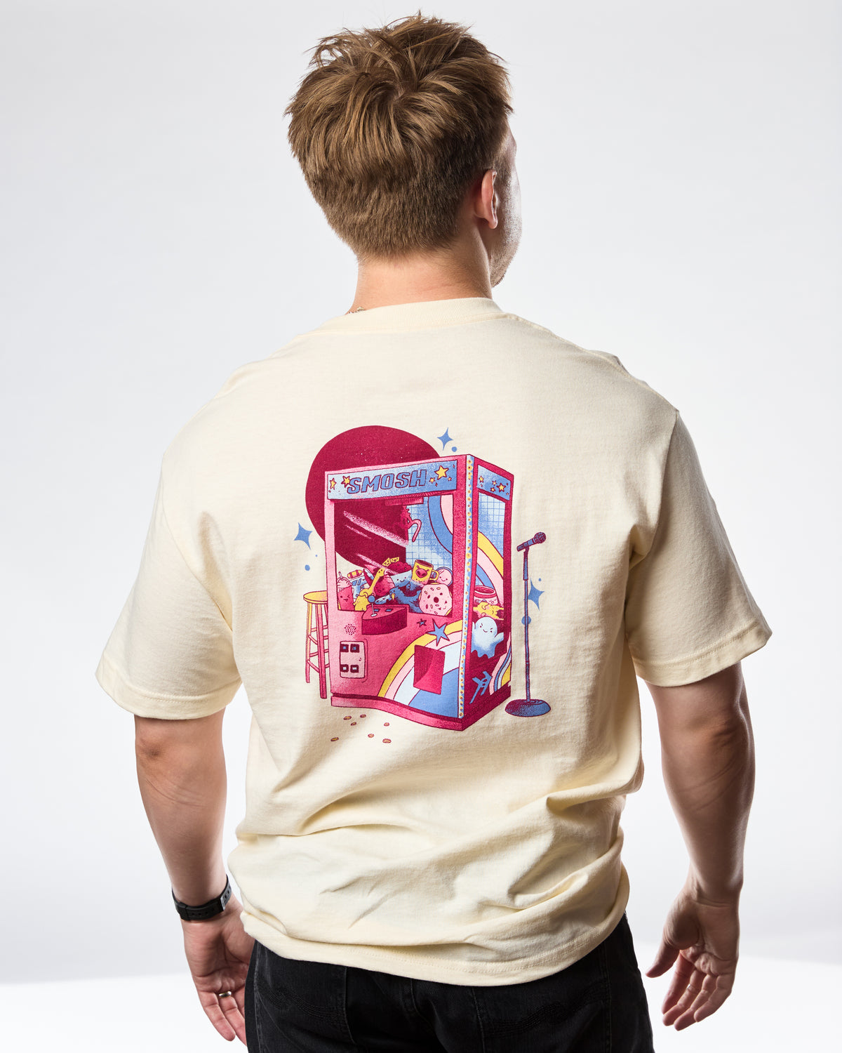 man wearing a cream t-shirt with 'SMOSH' text and stars on a white background back of shirt has a claw machine 