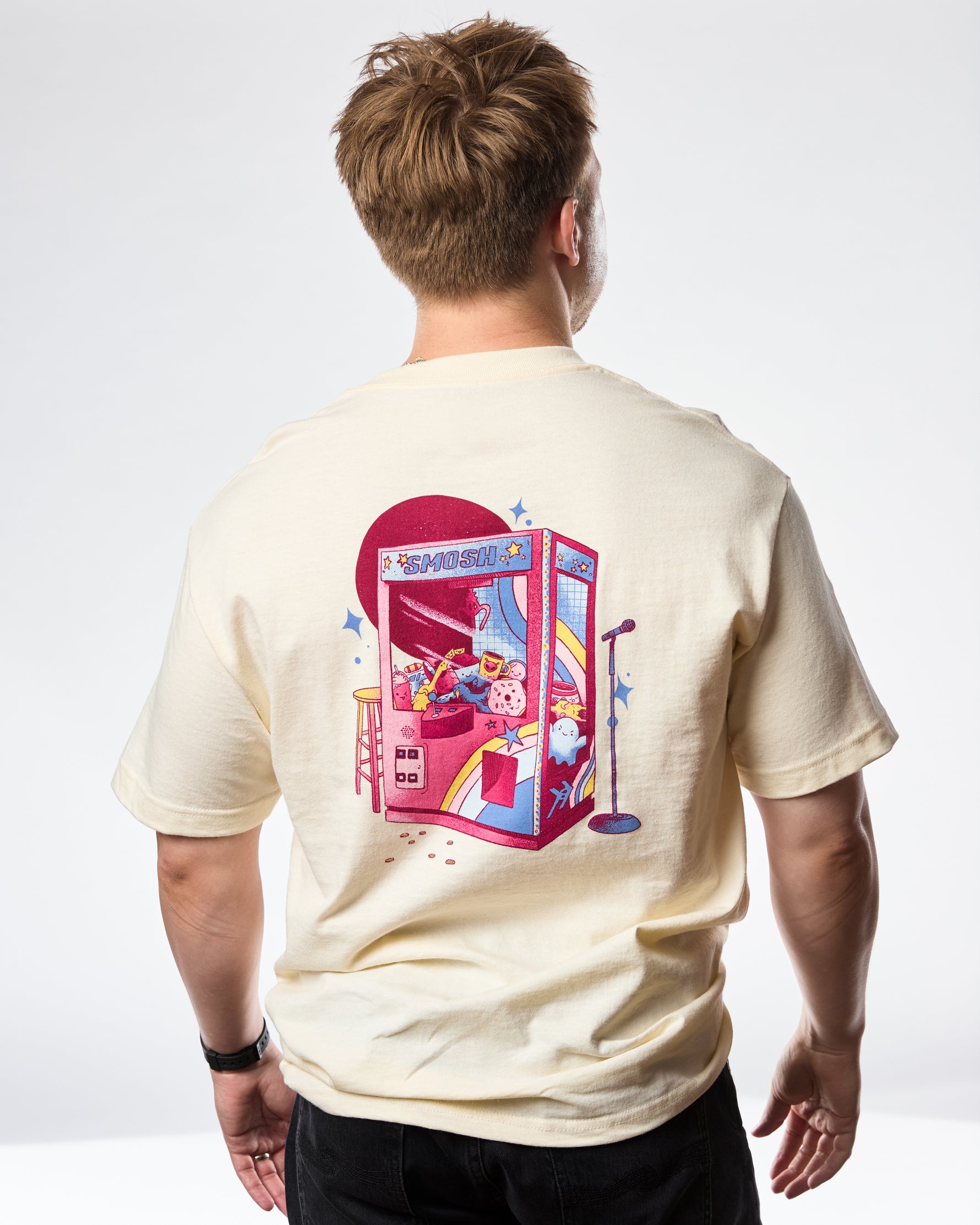 man wearing a cream t-shirt with 'SMOSH' text and stars on a white background back of shirt has a claw machine 