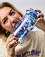 Person holding a blue water bottle with stickers, acting like she's biting water bottle 