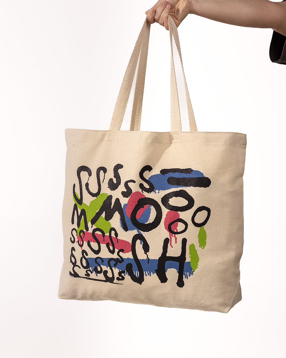 Beige tote bag with colorful Smosh text held by a hand on a white background