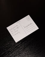 White postcard with handwritten text on a textured black surface